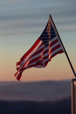 A vibrant US flag waves against a scenic sunset backdrop in Stowe, Vermont.